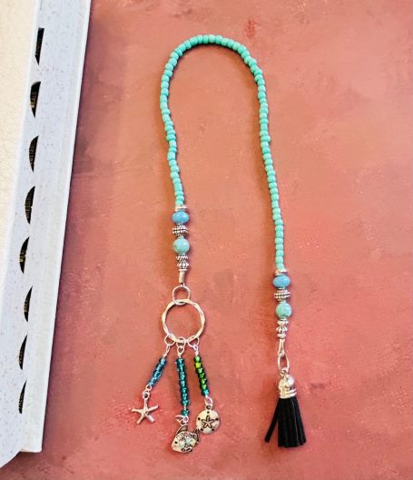 Turquoise Beaded Bookmark With Charms on a brown desk with a book